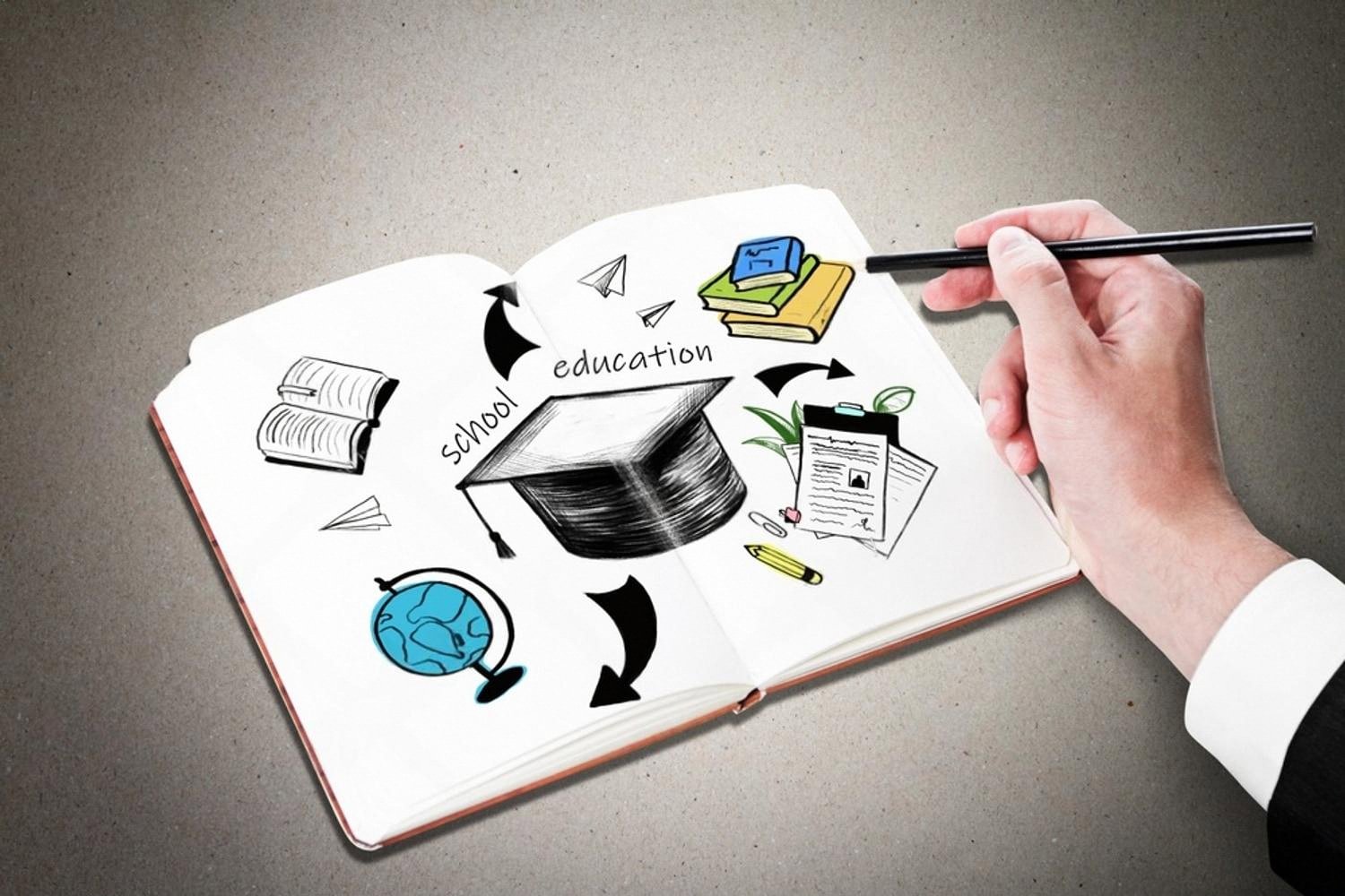 Open notebook with education and school sketches next to a hand holding a pencil